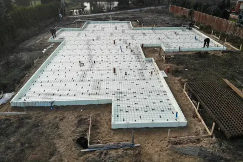 Budowa fundamentu punktowego pod dom szkieletowy. Betonowanie płyty fundamentowej zbrojonej siatką i rurkami.